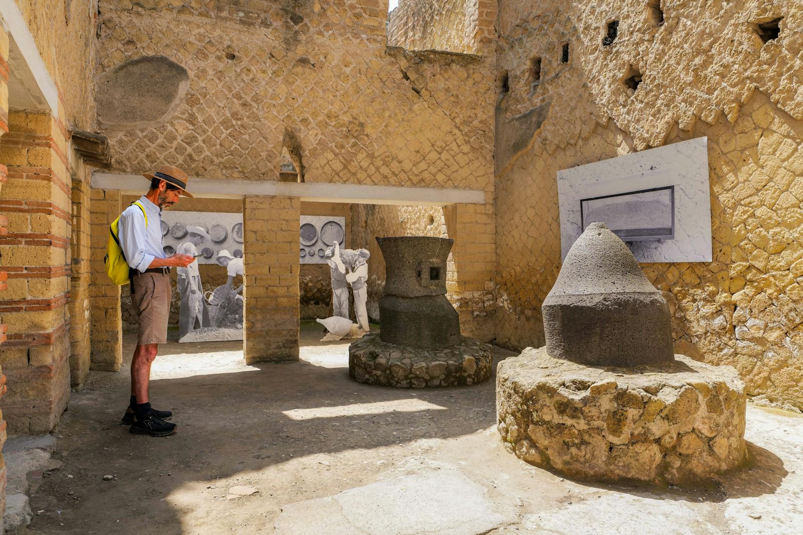 Visitor observing ancient millstones at Herculaneum