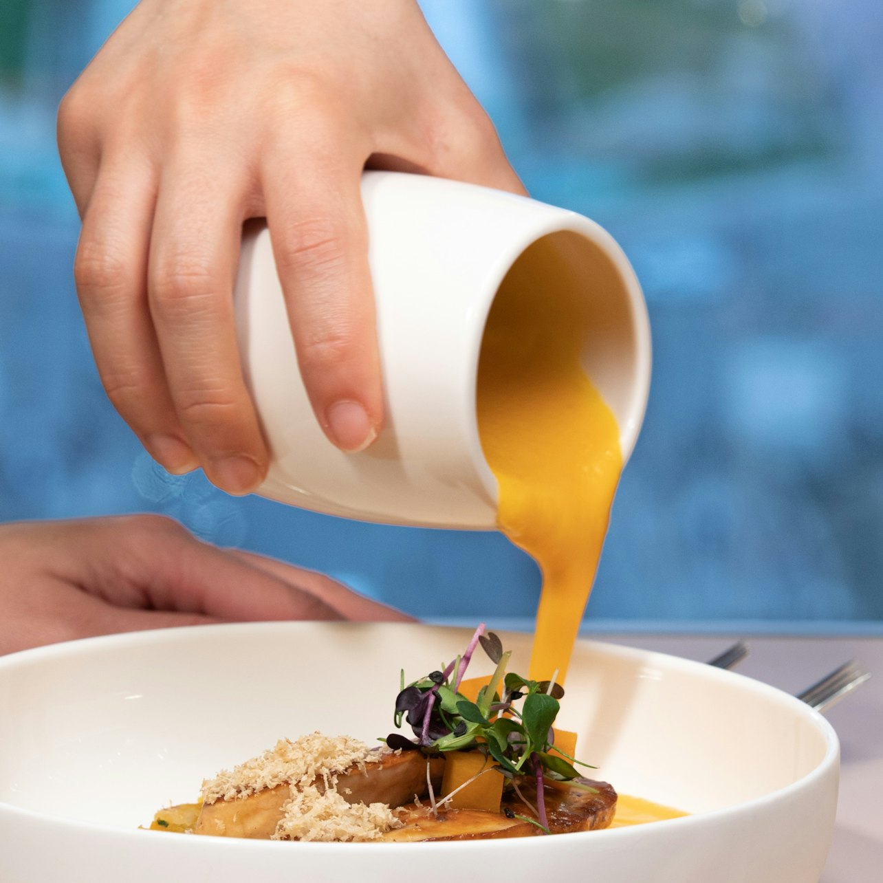 Eine Hand gießt goldene Sauce auf den Eiffelturm